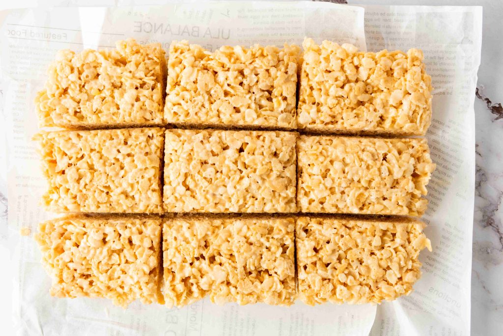 Nine Rice Krispie Treats, golden and rectangular, are arranged on parchment paper and cut into equal portions. With their textured surface from puffed rice cereal, they make perfect 4th of July treats.