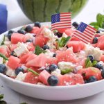 A festive Watermelon Blueberry Feta Salad, topped with fresh mint and tiny American flags, makes the perfect red white blue salad for your summer BBQ. Fresh mint leaves and a glimpse of juicy watermelon complete the scene.