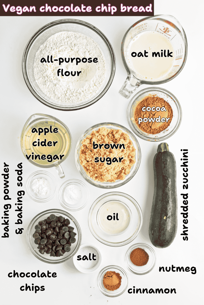 Top view of labeled ingredients for vegan chocolate chip zucchini bread, including flour, oat milk, cocoa powder, brown sugar, zucchini, oil, apple cider vinegar, chocolate chips, baking powder, baking soda, salt, nutmeg, and cinnamon.