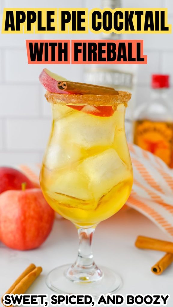 A glass of apple pie cocktail fireball with ice, garnished with an apple slice and cinnamon stick. Fresh apples, cinnamon sticks, and a Fireball whisky bottle sit in the background. Text reads Apple Pie Cocktail with Fireball—sweet, spiced, and boozy.