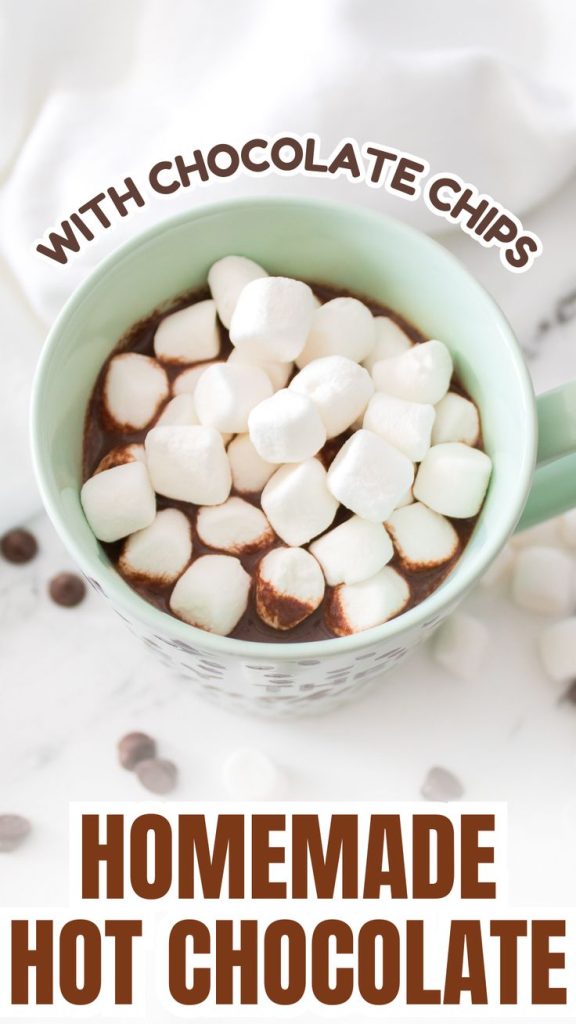 A mug of homemade hot chocolate with chocolate chips is topped with mini marshmallows and sits on a white surface, surrounded by extra chocolate chips. Text on the image reads WITH CHOCOLATE CHIPS and HOMEMADE HOT CHOCOLATE.