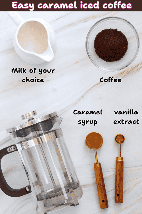 A marble surface displays how to make caramel iced coffee at home, featuring labeled ingredients: a jug of milk, a bowl of ground coffee, a French press, a spoon of caramel syrup, and a spoon of vanilla extract.