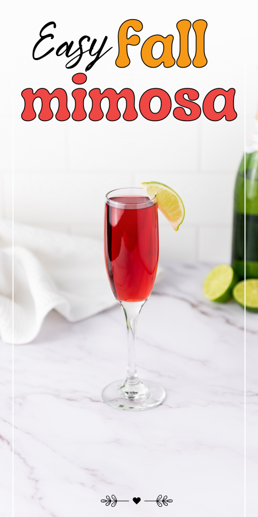 A glass of red mimosa made with cranberry juice is garnished with a lime wedge on a marble counter, surrounded by a wine bottle, sliced limes, and a white towel. Text above reads, “Easy Fall Mimosas with Cranberry Juice.”.