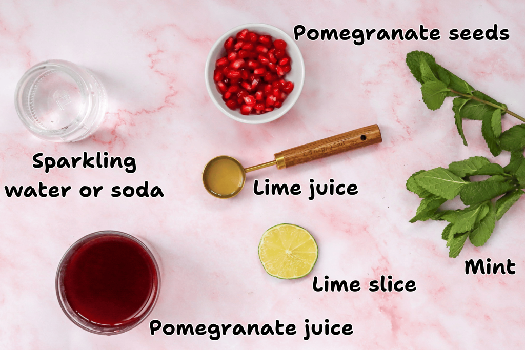 Flat lay for a Mocktail with Pomegranate Juice Recipe: sparkling water, pomegranate seeds, lime juice, a lime slice, fresh mint, and pomegranate juice arranged on a pink background with text labels for each ingredient.