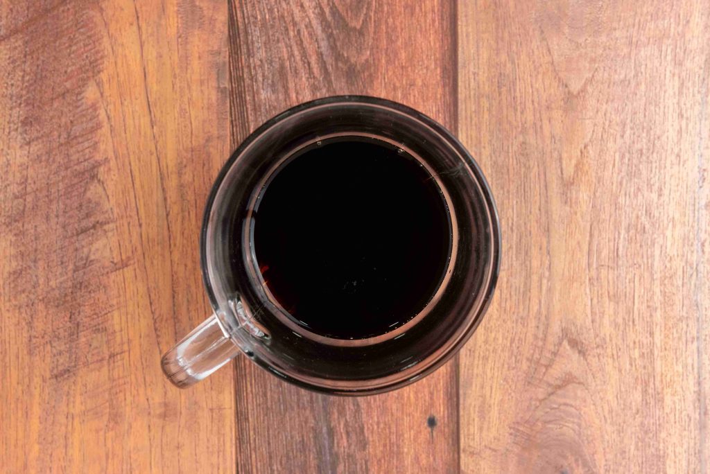 A top-down view of a clear glass mug filled with dark coffee, placed on a wooden surface with visible grain patterns—perfect inspiration for your next Christmas coffee or gingerbread latte recipe.
