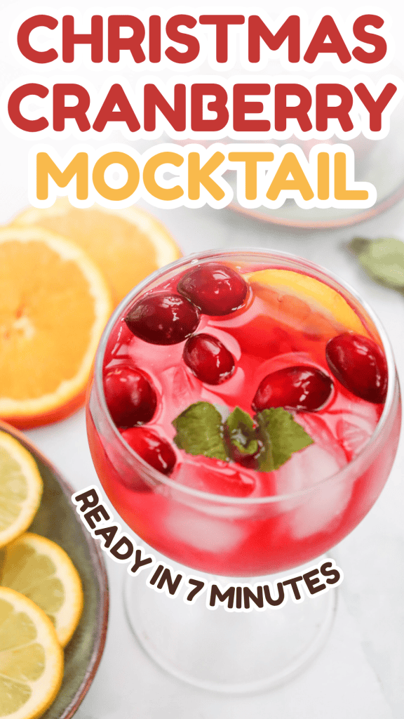 A festive cranberry Christmas mocktail garnished with cranberries and mint in a glass, surrounded by orange slices. Bold text reads “Christmas Cranberry Mocktail” and “Ready in 7 minutes.”.