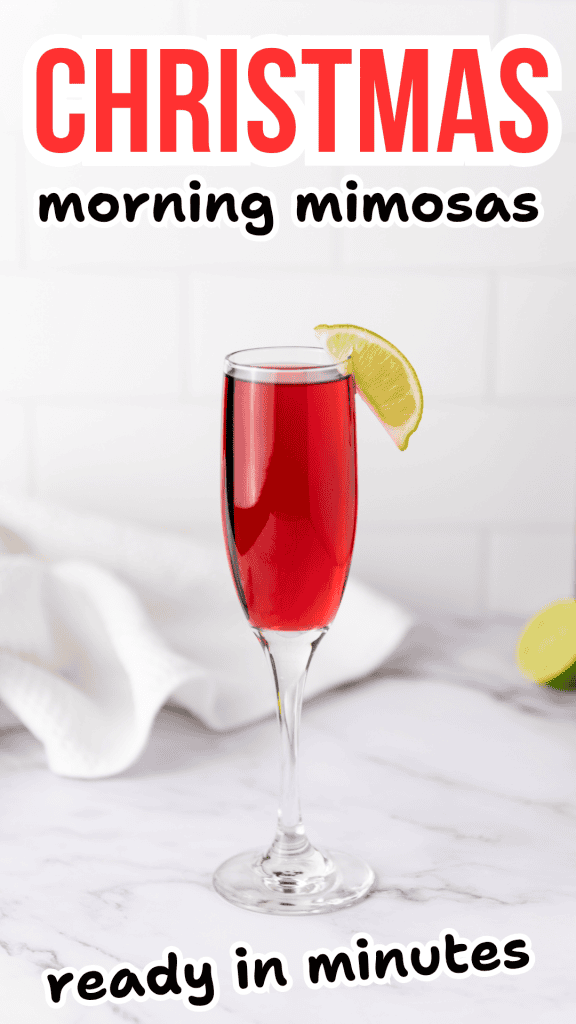 A glass of red Christmas morning mimosa with a lime wedge garnish sits on a counter, with text that reads CHRISTMAS morning mimosas ready in minutes. A white towel and lime are in the background.