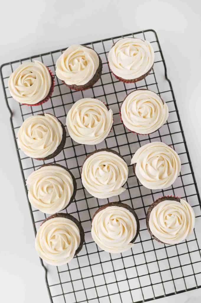 Twelve chocolate Christmas tree cupcakes with swirled white frosting are arranged neatly on a black wire cooling rack, viewed from above on a white background.