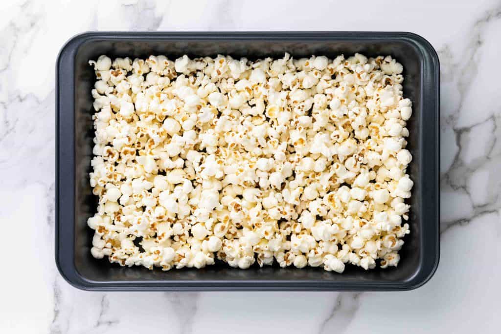A rectangular black baking pan filled with holiday popcorn sits on a white marble surface.