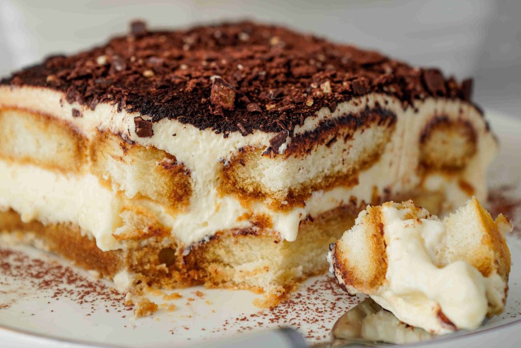 A close-up of a sliced Christmas tiramisu dessert showing layers of coffee-soaked ladyfingers, creamy mascarpone, and cocoa powder, with a spoonful resting on the plate.