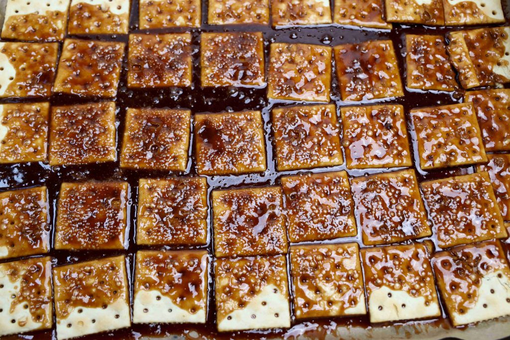 A close-up of square crackers laid out in rows, topped with a glossy caramel or toffee coating, creates an irresistible Valentine’s Day Bark—perfectly crafted for a festive dessert or sweet snack.