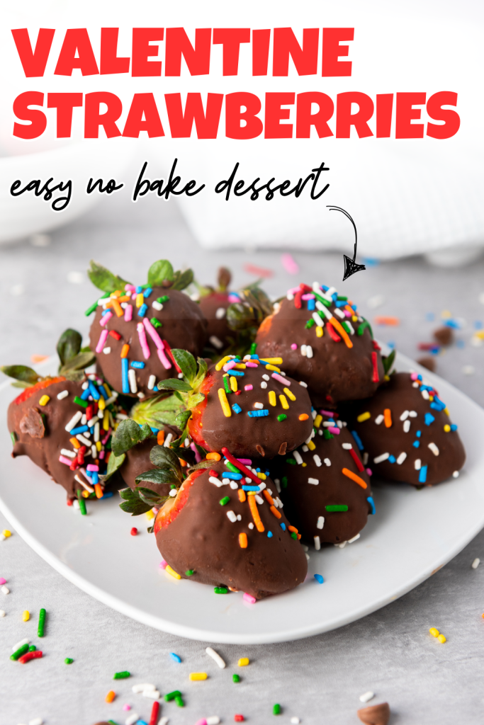 A plate of Valentine's Day Chocolate Covered Strawberries topped with colorful sprinkles sits on a gray surface. Text above reads Valentine Strawberries, easy no bake dessert. Some sprinkles are scattered around the plate.