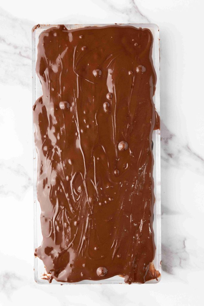 A rectangular slab of Valentine's Day chocolate candy with a glossy, uneven surface rests on a white marble background.