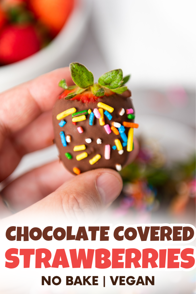 A hand holds a dairy-free chocolate covered strawberry topped with colorful sprinkles. In the background, strawberries are visible. Text at the bottom reads: Chocolate Covered Strawberries. No Bake | Vegan.