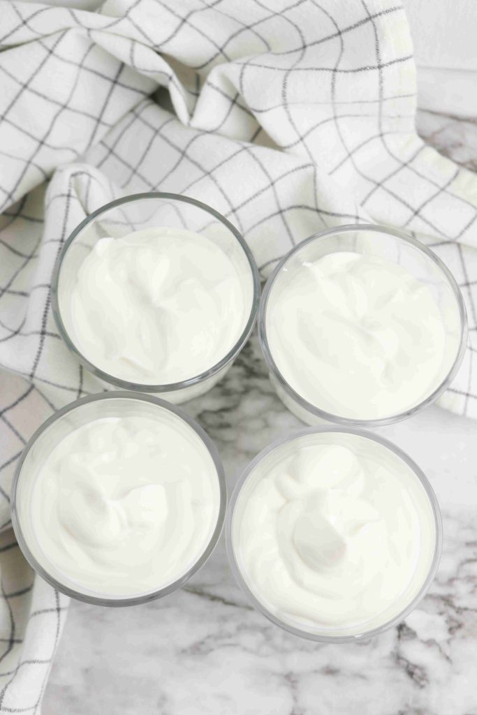 Four glass bowls filled with Oreo Yogurt Cups are arranged on a marble surface, with a white and black checkered cloth draped in the background.