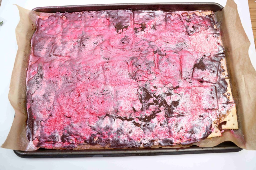 A large rectangular sheet of Valentine’s Day Bark with a shiny red and chocolate brown glazed topping sits on a parchment-lined baking tray.