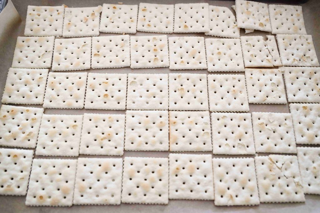 A close-up view of several rows of square, salted crackers arranged neatly in a grid pattern on a flat surface, perfect as a base for creating festive Valentine’s Day Bark treats.
