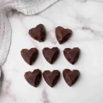 Eight heart-shaped dark chocolates, perfect as Valentine's Day chocolate candy, arranged in three rows on a white marble surface beside a white textured kitchen towel with blue stripes.