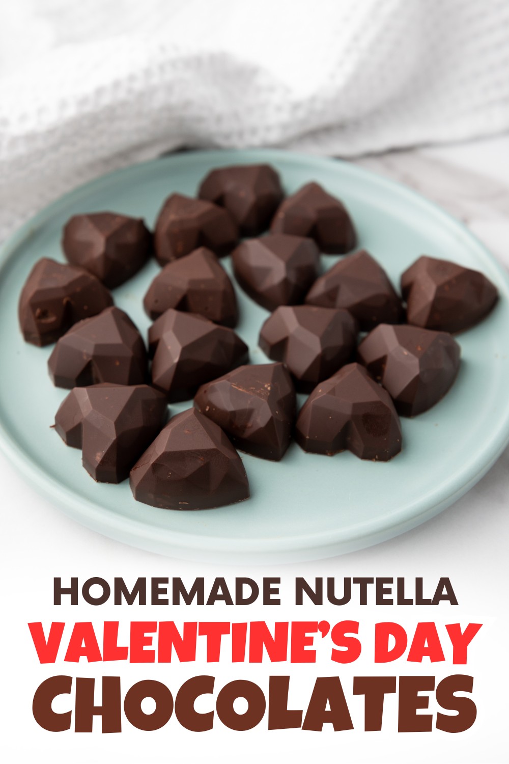 A light blue plate holds several diamond-shaped dark chocolates. The image includes text that reads: Homemade Nutella Valentine's Day chocolate candy. A white textured cloth is in the background.