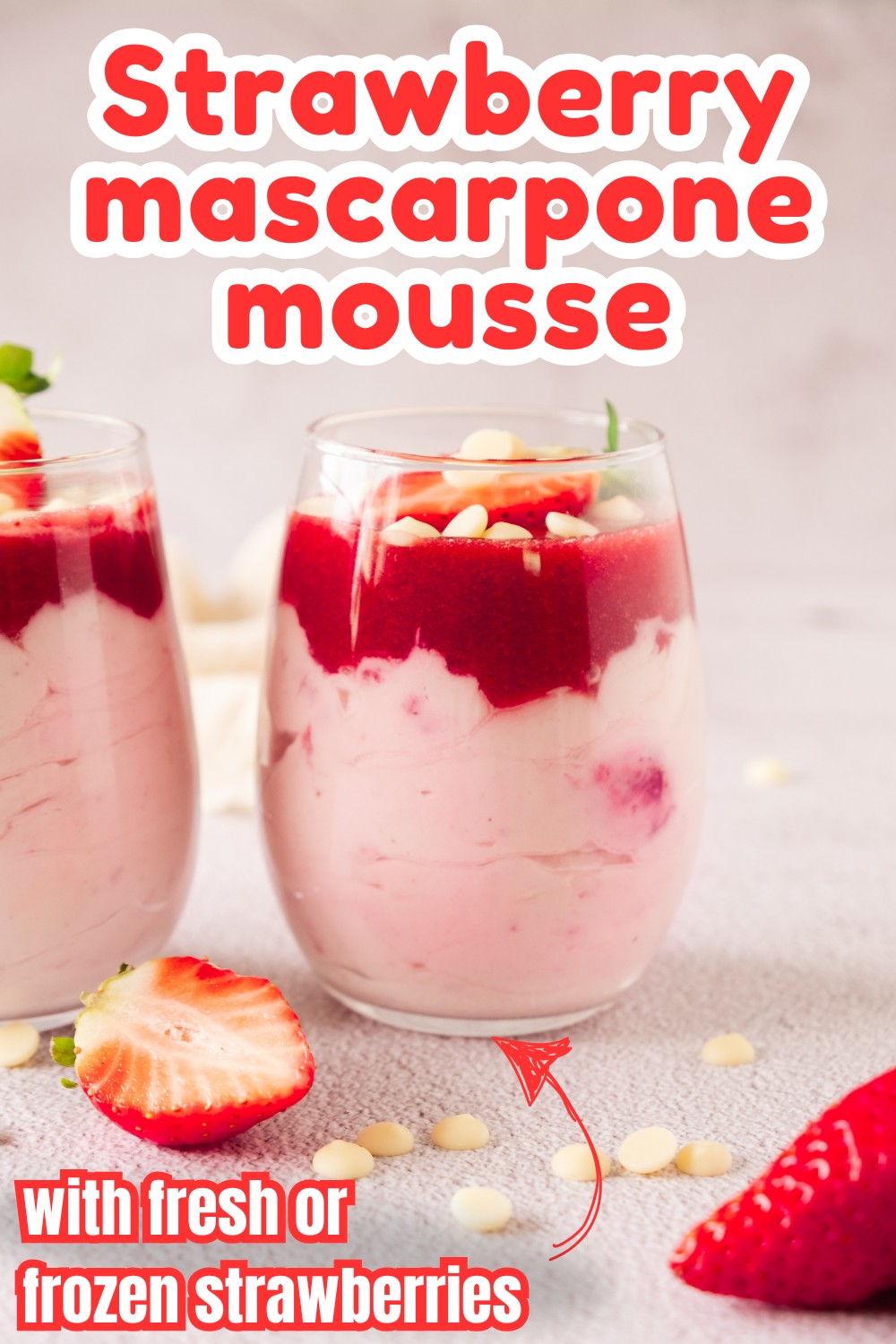 Two glasses of strawberry mascarpone dessert mousse, topped with strawberry sauce and white chocolate chips, sit on a light surface. A sliced strawberry and white chocolate chips are scattered around. Text reads “Strawberry mascarpone mousse.”.
