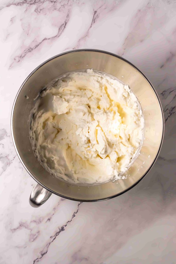 A metal mixing bowl filled with whipped cream sits on a white marble surface, ready to top your Old Fashioned Strawberry Shortcake Recipe.
