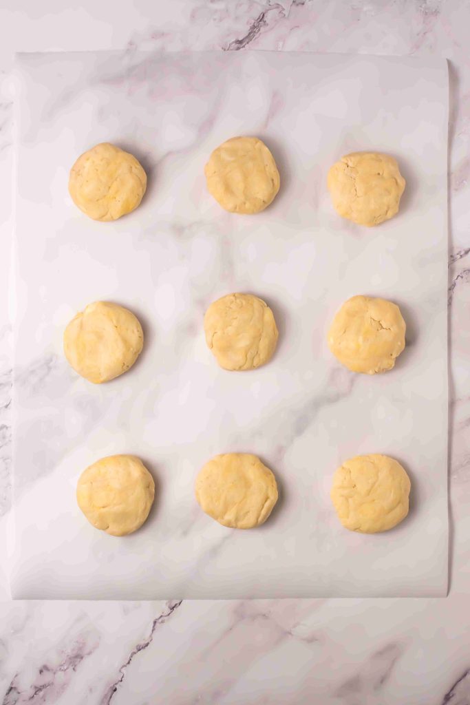 Nine round, unbaked cookie dough balls are arranged in a grid pattern on a sheet of parchment paper over a marble surface, reminiscent of preparing an Old Fashioned Strawberry Shortcake Recipe from scratch.