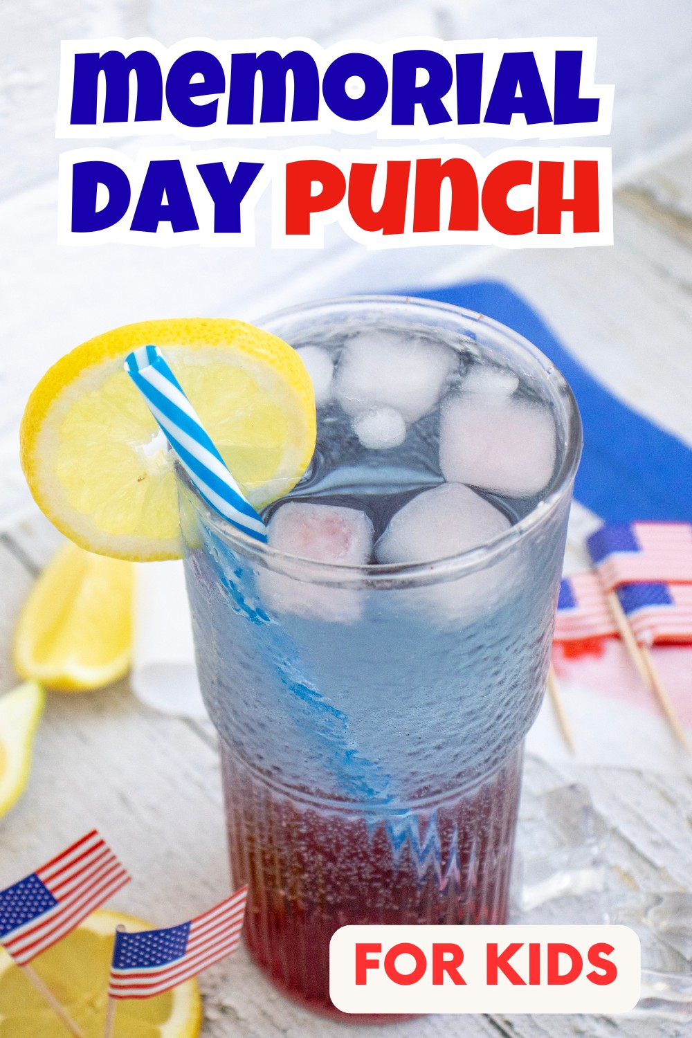 A glass of red and blue layered Memorial Day Punch with ice, a lemon slice, and a blue striped straw. Small American flags and lemon wedges sit nearby. Text reads Memorial Day Punch for Kids.