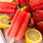 Strawberry popsicles arranged on ice with fresh strawberries and lemon slices around them. These vibrant treats are the perfect result of an Easy Strawberry Popsicles Recipe, making summer snacking simple and refreshing.