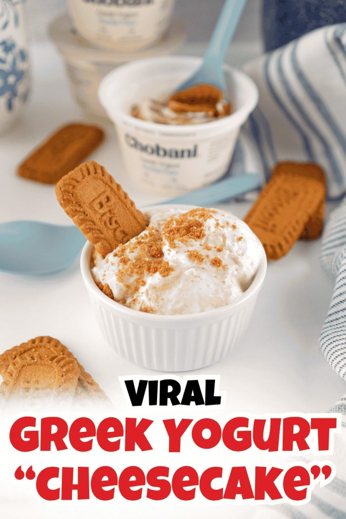 A small white bowl of Greek yogurt cheesecake topped with cookie crumbs and a biscuit, inspired by the biscoff yogurt recipe, with yogurt containers, cookies, and blue spoons in the background. Text: Viral Greek Yogurt Cheesecake.