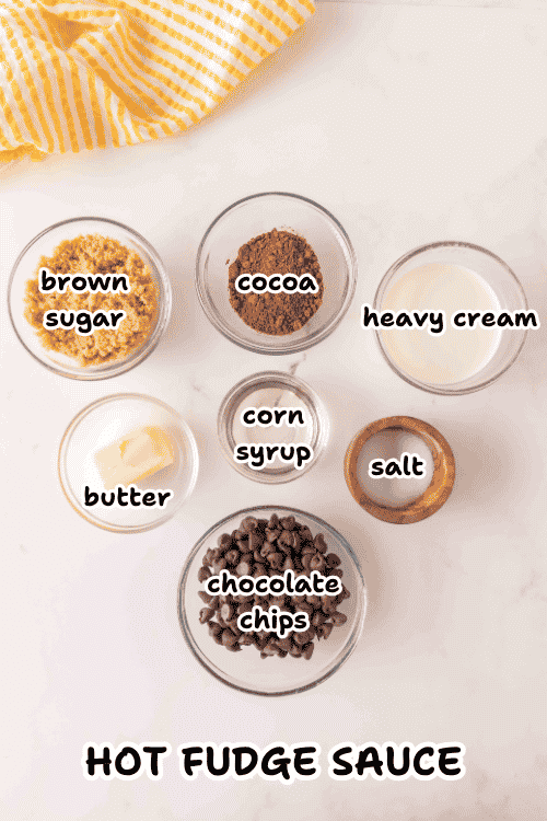 Six labeled bowls contain brown sugar, cocoa, heavy cream, butter, corn syrup, salt, and chocolate chips, all arranged on a white surface—just the ingredients you need for a delicious homemade hot fudge sauce. Text at the bottom reads HOT FUDGE SAUCE.