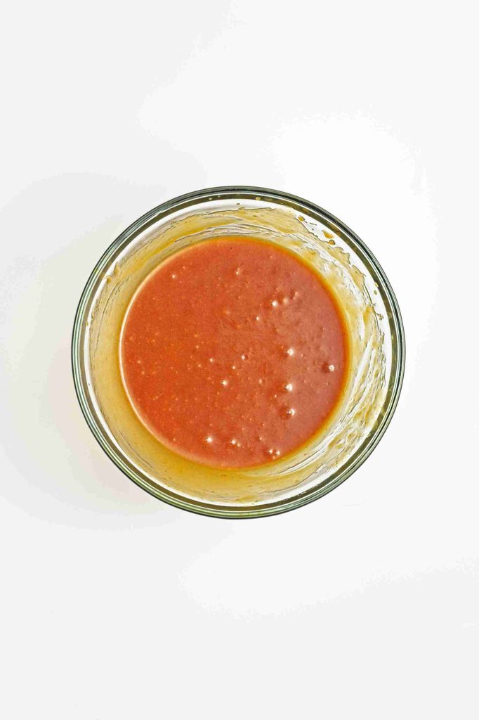 A glass bowl filled with reddish-orange sauce or dressing, viewed from above, on a white background—perfect for drizzling over fresh salads or as a delightful dip alongside vegan pumpkin chocolate chip cookies.