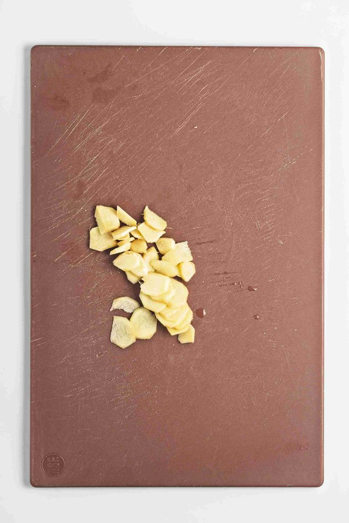 Chopped garlic pieces in a small pile on the center of a brown cutting board with a white background, ready to be infused into dishes or paired with flavors like gingerbread syrup for a creative twist.