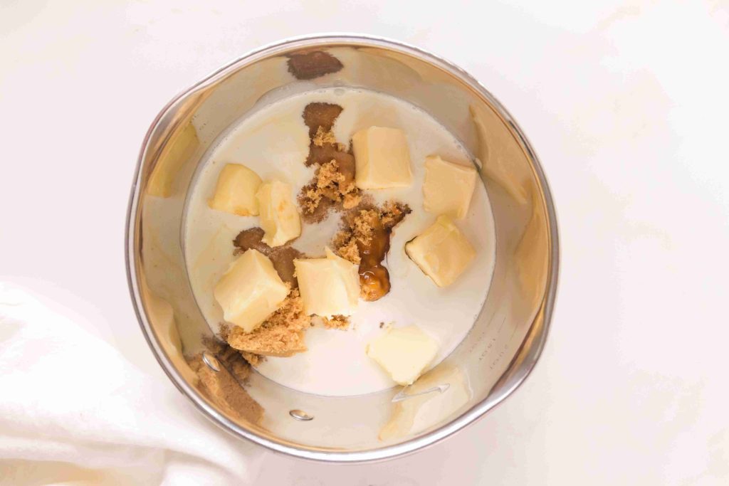 A metal bowl contains cubes of butter, brown sugar, and cream, ready to be mixed together on a white surface—the perfect start for a classic butterscotch sauce recipe.