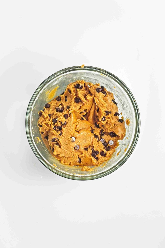 A glass bowl filled with vegan pumpkin chocolate chip cookie dough sits on a white surface.