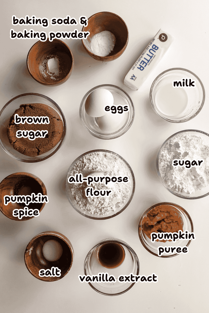 Top-down view of labeled baking ingredients for pumpkin cookies with icing in bowls on a white surface, including pumpkin purée, brown sugar, eggs, flour, pumpkin spice, and more.