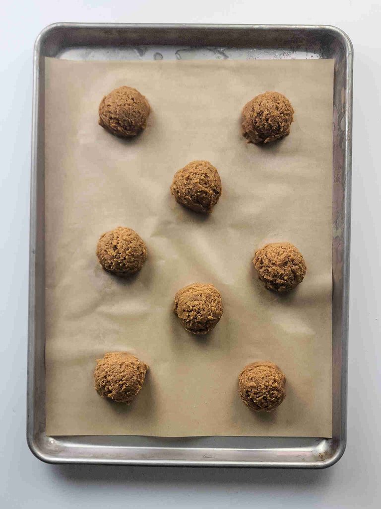 Nine unbaked pumpkin cookies with icing are evenly spaced on a parchment-lined baking sheet, ready to be baked.