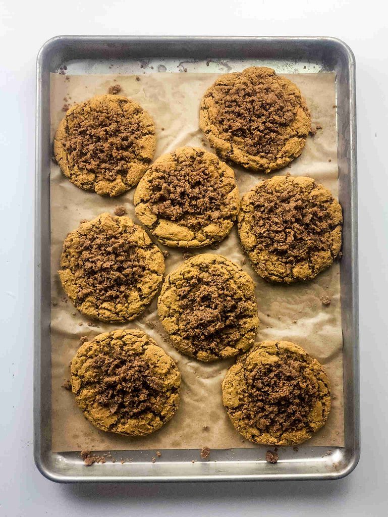 A baking sheet with eight large pumpkin coffee cake cookies, crumb-topped and arranged on parchment. The cookies have a golden-brown color and are evenly spaced on the tray.
