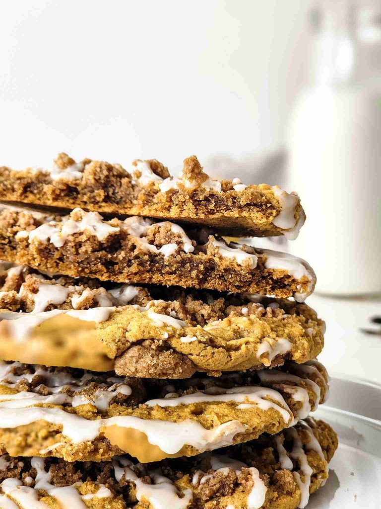 A close-up of a stack of crumbly pumpkin cookies with icing, drizzled with white glaze, with a blurred bottle of milk in the background.