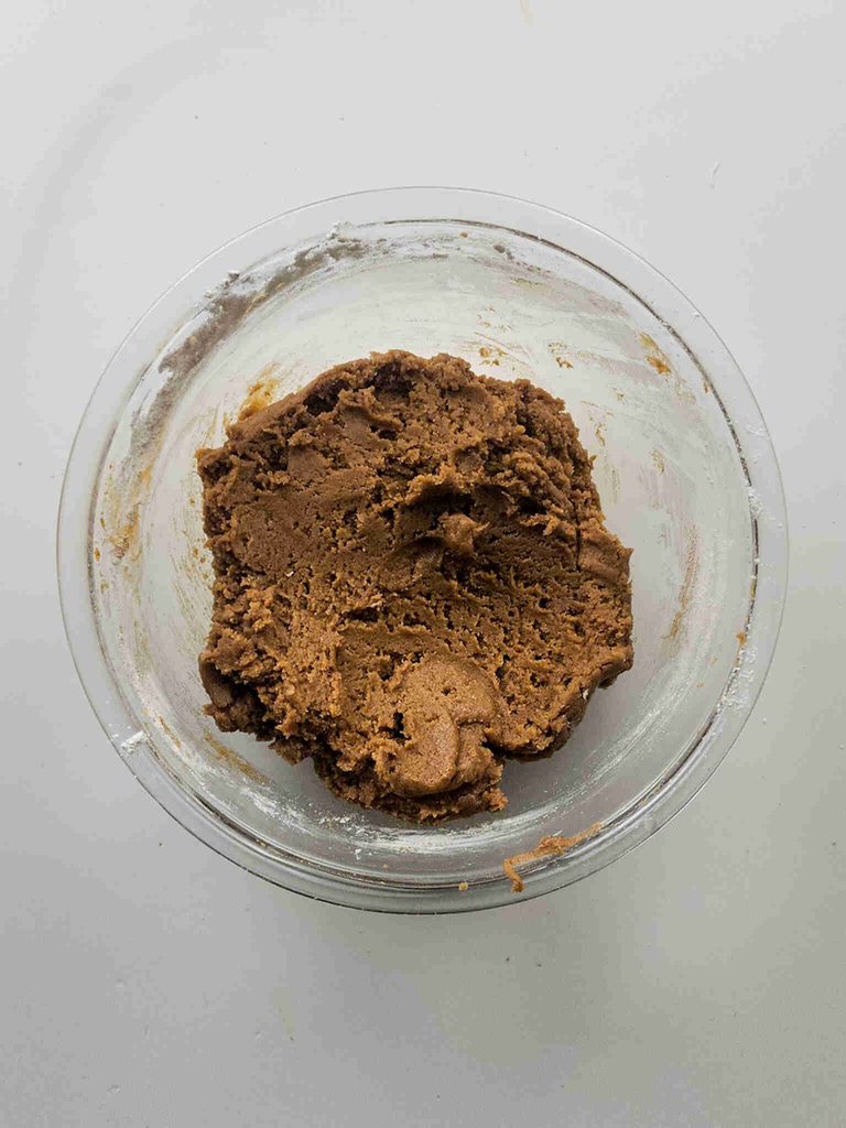 A clear glass bowl filled with brown pumpkin cookie dough for pumpkin cookies with icing sits on a white surface, viewed from above.