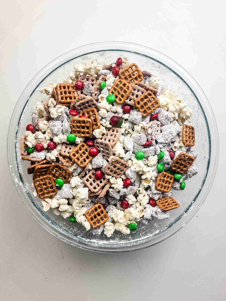 A glass bowl filled with reindeer munch, a snack mix of popcorn, pretzels, powdered sugar-coated cereal, and red and green M&M candies.