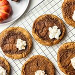 Pumpkin Pie Cookies with whipped cream dollops are cooling on a wire rack. A decorative pumpkin and a white plate are partially visible in the top left corner.