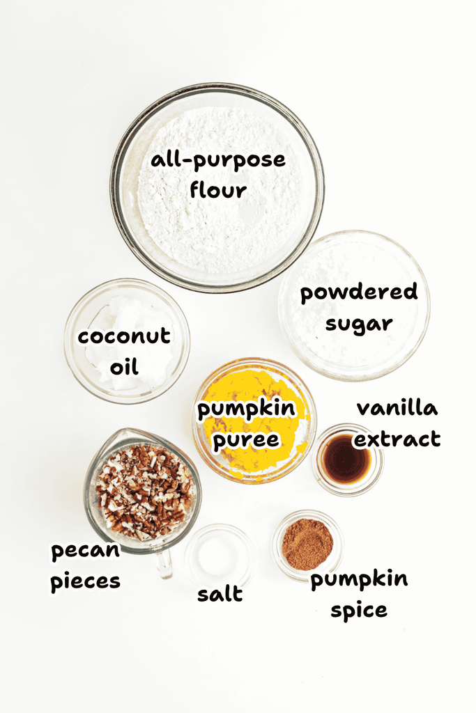 Seven bowls and cups filled with labeled baking ingredients for vegan snowball cookies—flour, powdered sugar, coconut oil, pumpkin puree, pecans, vanilla, salt, and pumpkin spice—arranged on a white background.