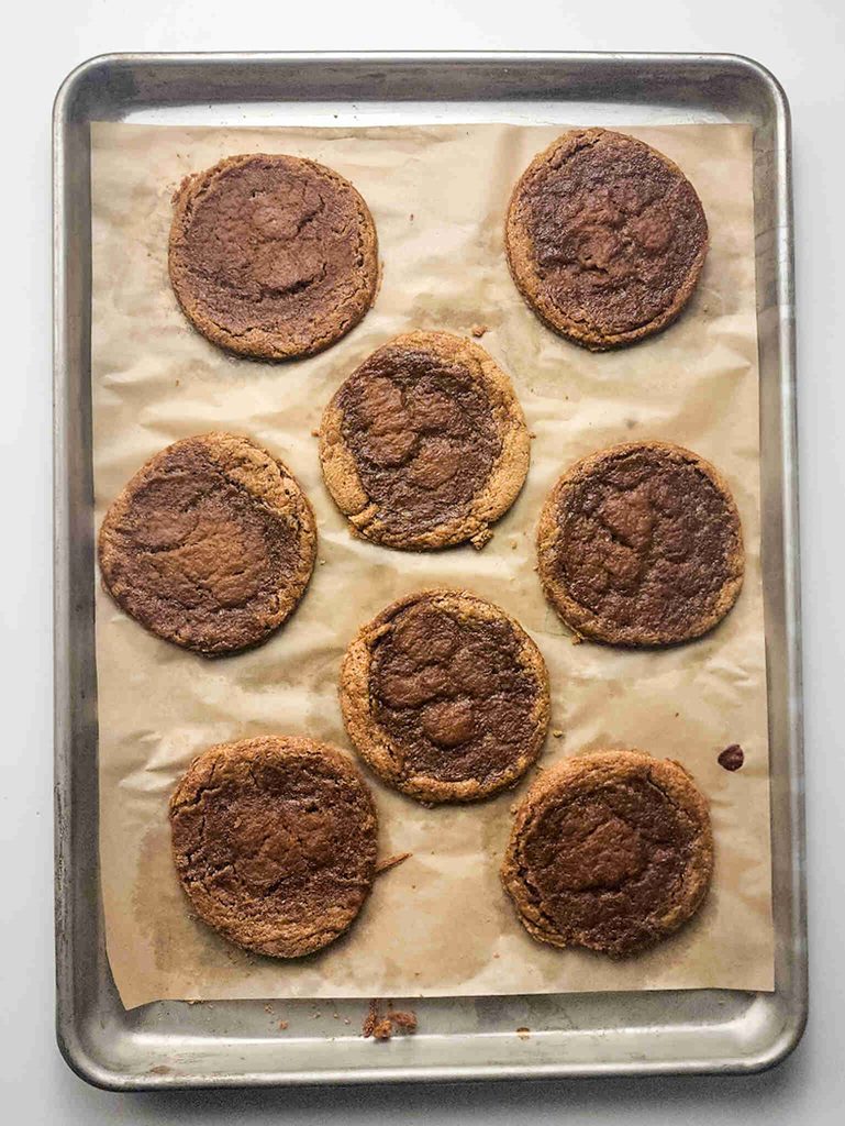 Eight large pumpkin pie filled cookies on a baking sheet lined with parchment paper, arranged in two columns.