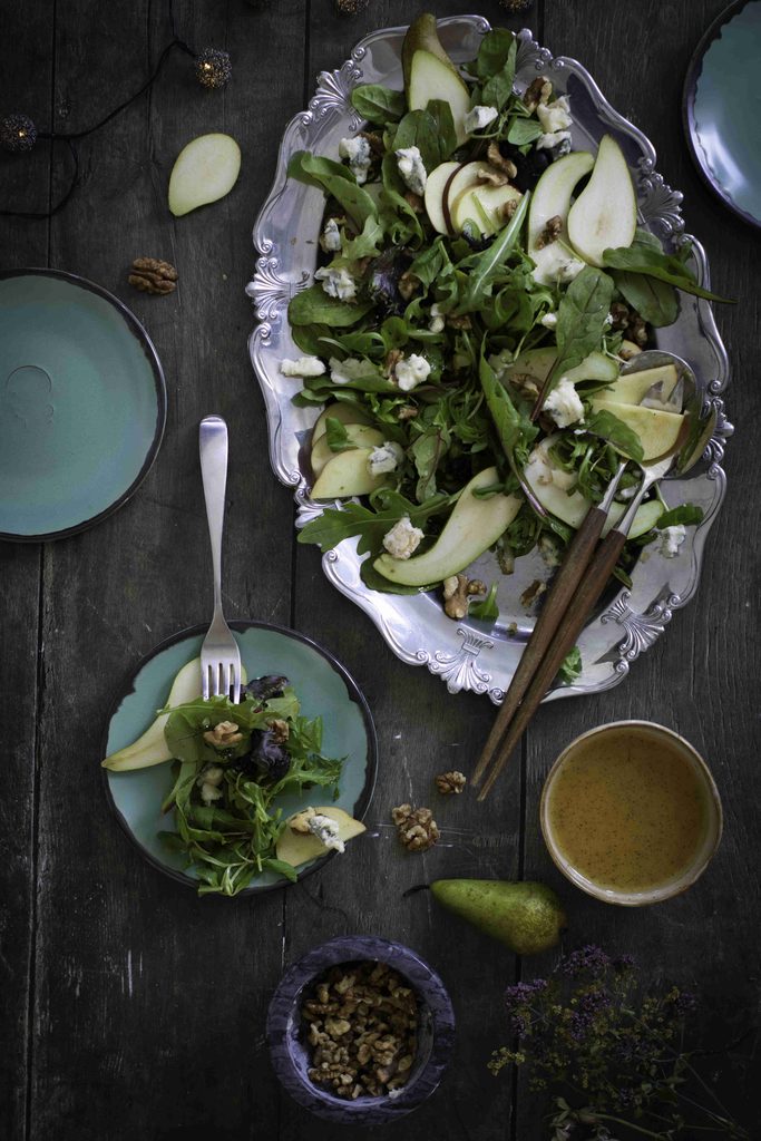 An easy Thanksgiving salad of arugula, sliced pears, walnuts, and blue cheese on a silver platter, with a serving on a small plate and a bowl of dressing nearby.