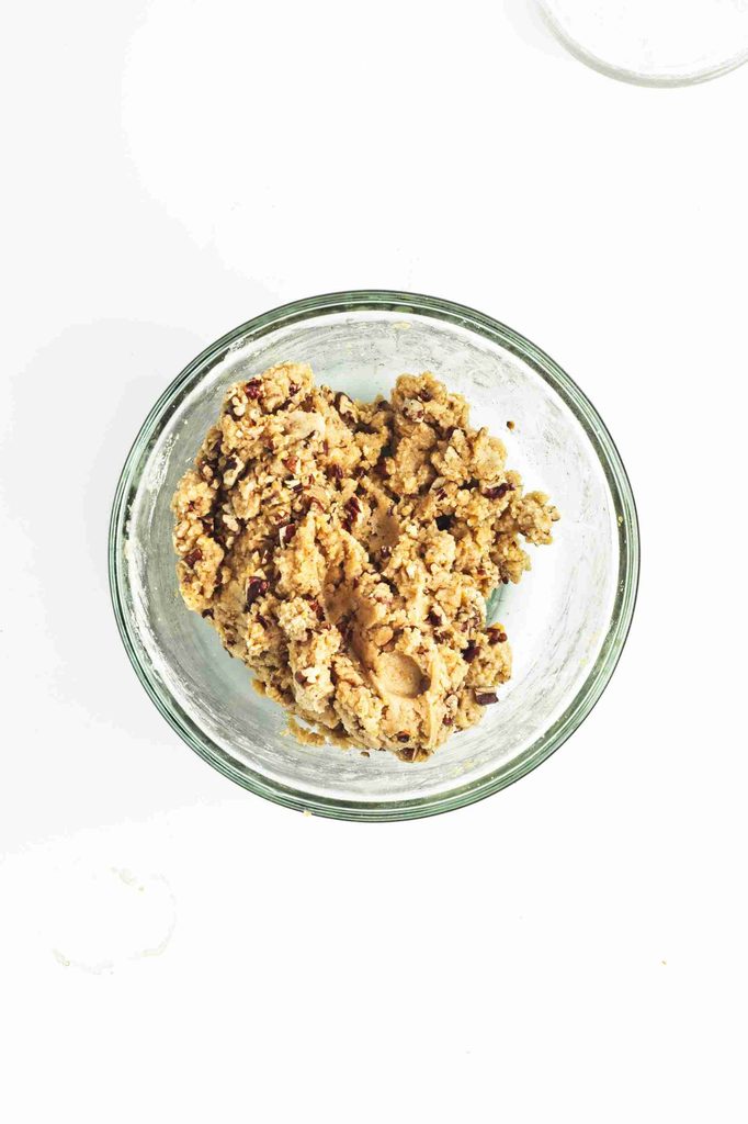 A glass bowl filled with chunky cookie dough for vegan snowball cookies mixed with pecans, viewed from above on a white background.